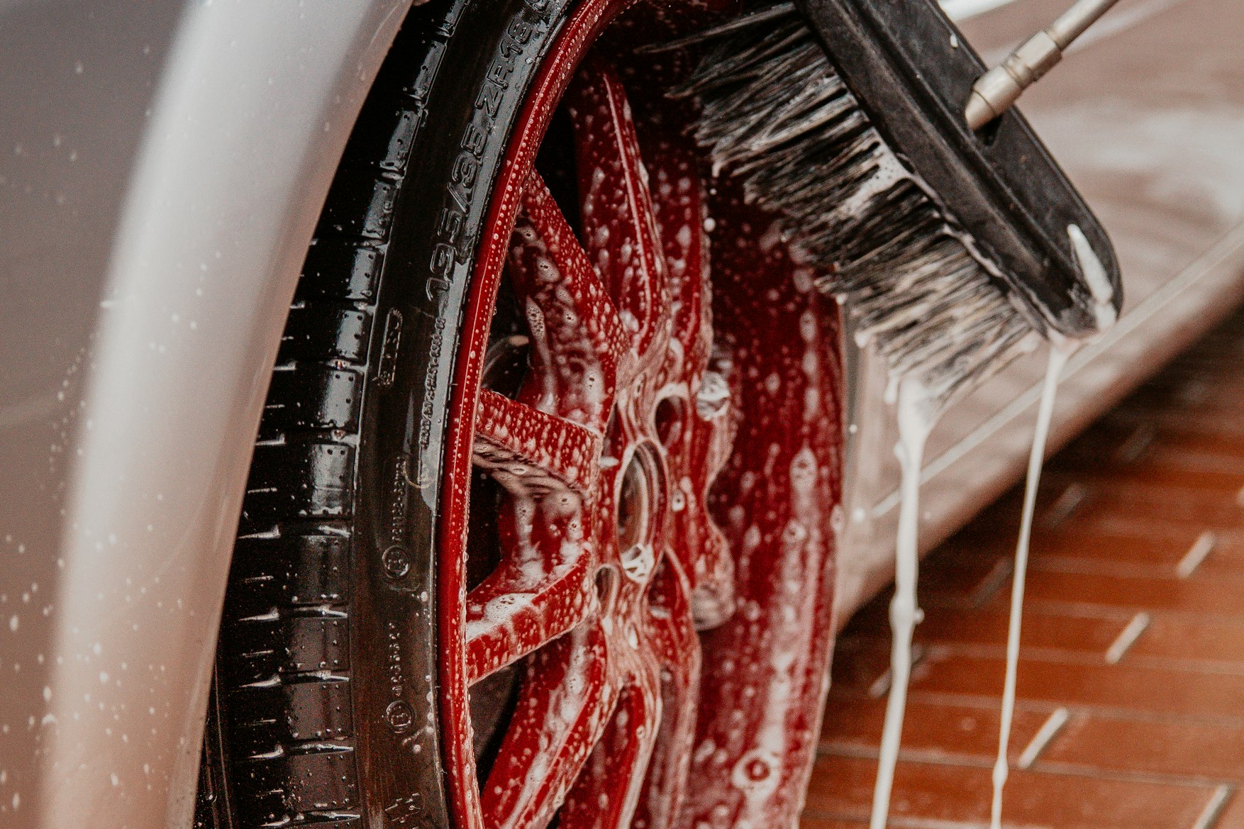 Close up of a car wheel and tire covered in wash foam, a detailing brush working the rim