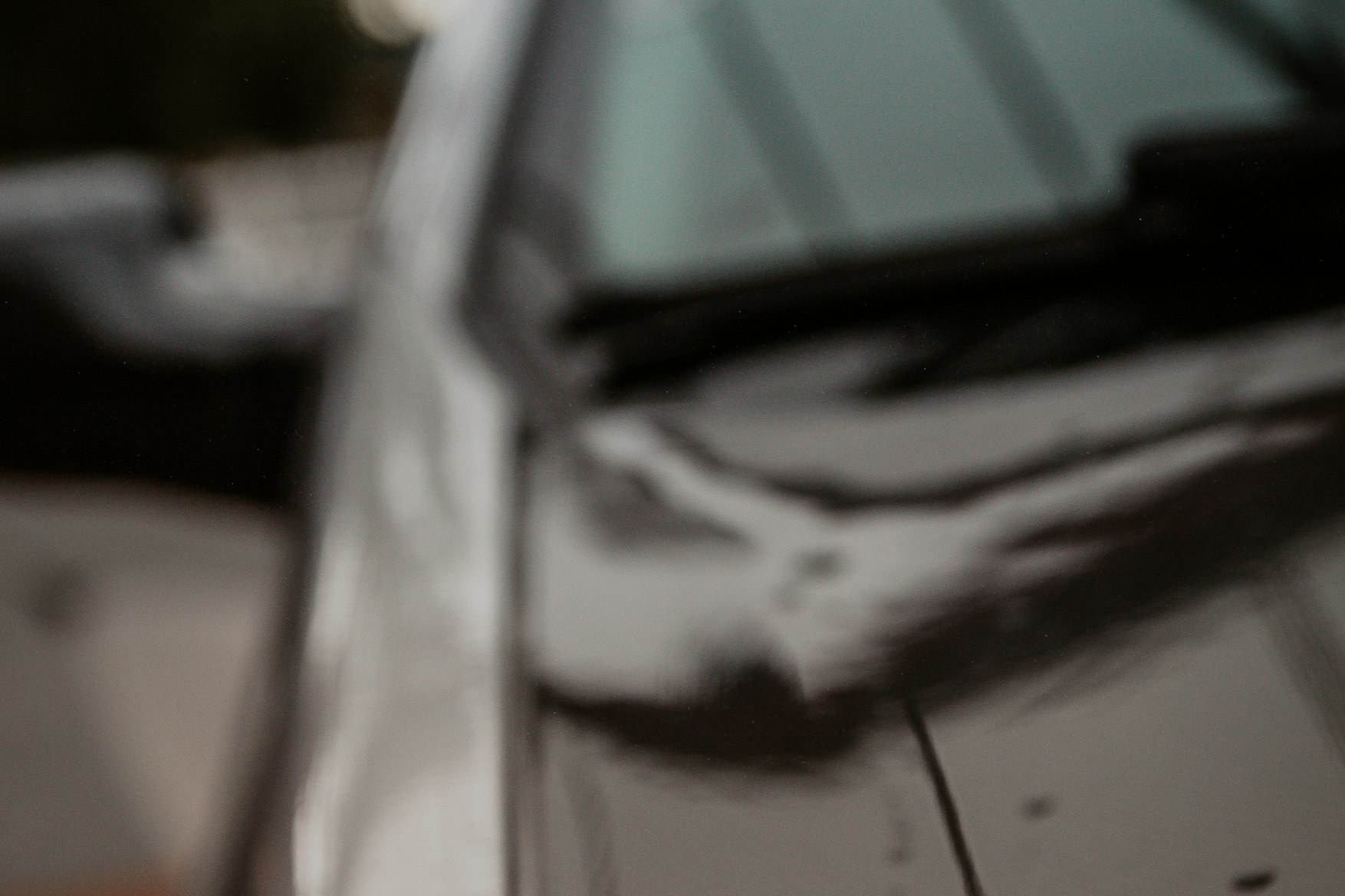 Water beaded across a dark car hood after a wash, shot close up with the background out of focus